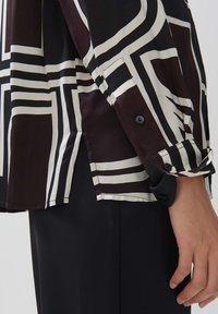 Black and white patterned long-sleeve shirt with a smooth texture, featuring a buttoned cuff and side slits for ease of movement.