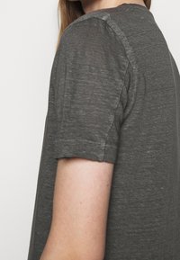 Camicetta grigia a maniche corte realizzata in tessuto leggero, con una vestibilità comoda e scollatura tonda; cuciture visibili sulle maniche.