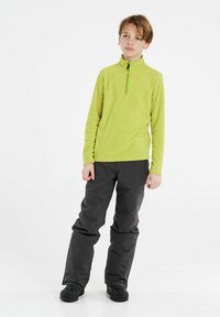 Pullover in pile verde con zip a metà, pantaloni isolati neri e stivali impermeabili neri, progettati per attività all'aperto.