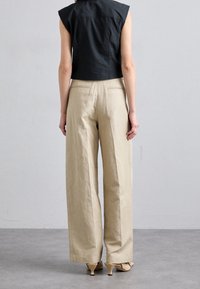 Top negro corto con acentos en los hombros, combinado con pantalones beige holgados. Los pantalones cuentan con una tela texturizada y bolsillos laterales.