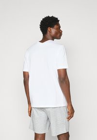 Hvid kortærmet t-shirt med rund hals, parret med lysegrå shorts. Cotton materiale, afslappet pasform og glat tekstur.