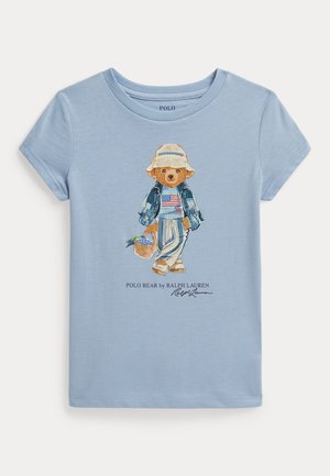 T-shirt bleu clair à manches courtes avec un dessin d'ours portant un chapeau, une veste en jean et un pantalon rayé, tenant un panier de raisins.