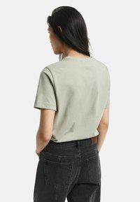 Lichtgroene katoenen t-shirt met een ronde hals en korte mouwen, gedragen met zwarte spijkerbroeken met twee achterzakken en een bruine leren label.