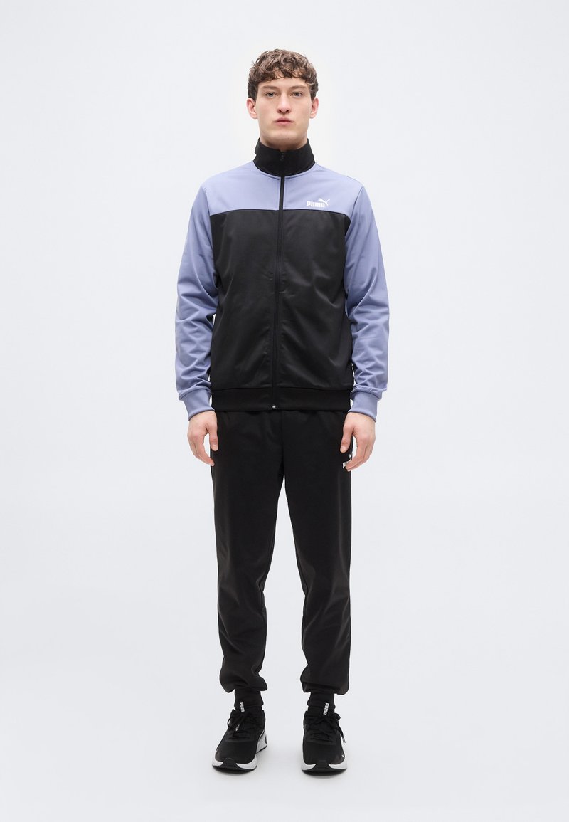 Αθλητική ζακέτα σε μαύρο και λιλά, με ψηλό γιακά και κλείσιμο με φερμουάρ. Ομαλό ύφασμα, συνδυασμένο με μαύρο παντελόνι και αθλητικά παπούτσια σε αντίστοιχο χρώμα.