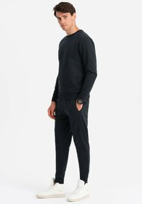Svart sweatshirt och matchande sweatpants i mjukt material, med ribbade ärmslut och sidofickor. Bärs med vita höga sneakers.