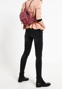 Läderryggsäck i dämpad rosa, med justerbara axelremmar, framficka och rundad form. Bärs med figurnära svarta jeans och ankelstövlar.