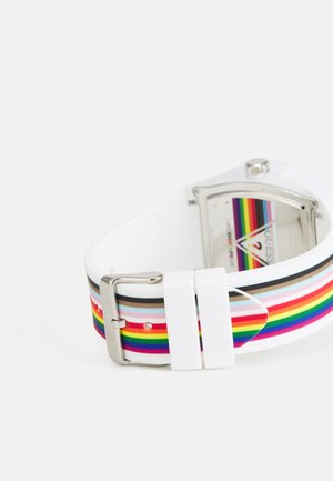 Pestrobarevné pruhované hodinky s bílým silikonovým náramkem a stříbrnou sponou, mající obdélníkový ciferník a živé mnohobarevné vzory.