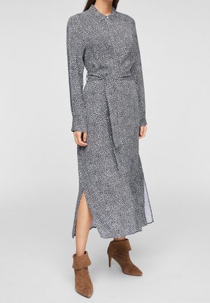 Femme portant une robe midi à manches longues noire et blanche à motifs, avec des fentes sur les côtés, et des bottines marron en daim à talons.