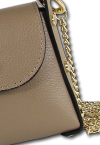 Sac en cuir beige avec une surface texturée, arborant une bandoulière en chaîne dorée et un bord noir le long des contours. Rabat de fermeture visible.