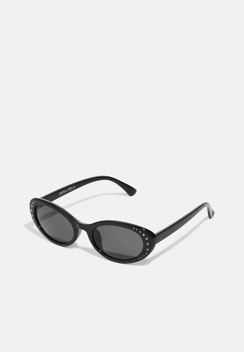 Black sunglasses with oval lenses, embellished with small rhinestones along the upper edge, featuring a sleek plastic frame and arms.