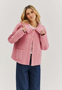 Růžová prošívaná bunda s velkým límcem, zapínáním na knoflíky a dvěma předními kapsami. Látka má strukturovaný, žebrovaný vzor. Nositá přes bílý top.