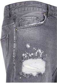 Jeans de mezclilla gris con detalles desgastados, que presentan bordes deshilachados y un gran corte en el muslo, complementados con herrajes metálicos.