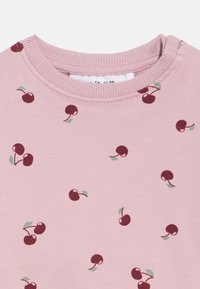 Tissu rose avec de petites illustrations de cerises rouge foncé éparpillées, accompagnées de feuilles vertes, et un col rond côtelé en haut.