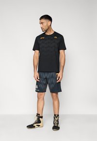 Μαύρο αθλητικό μπλουζάκι με υφή γεωμετρικού σχεδίου, συνδυασμένο με μαύρο σορτς που διαθέτει γκρι διακοσμητικές λεπτομέρειες και μικρό λογότυπο.