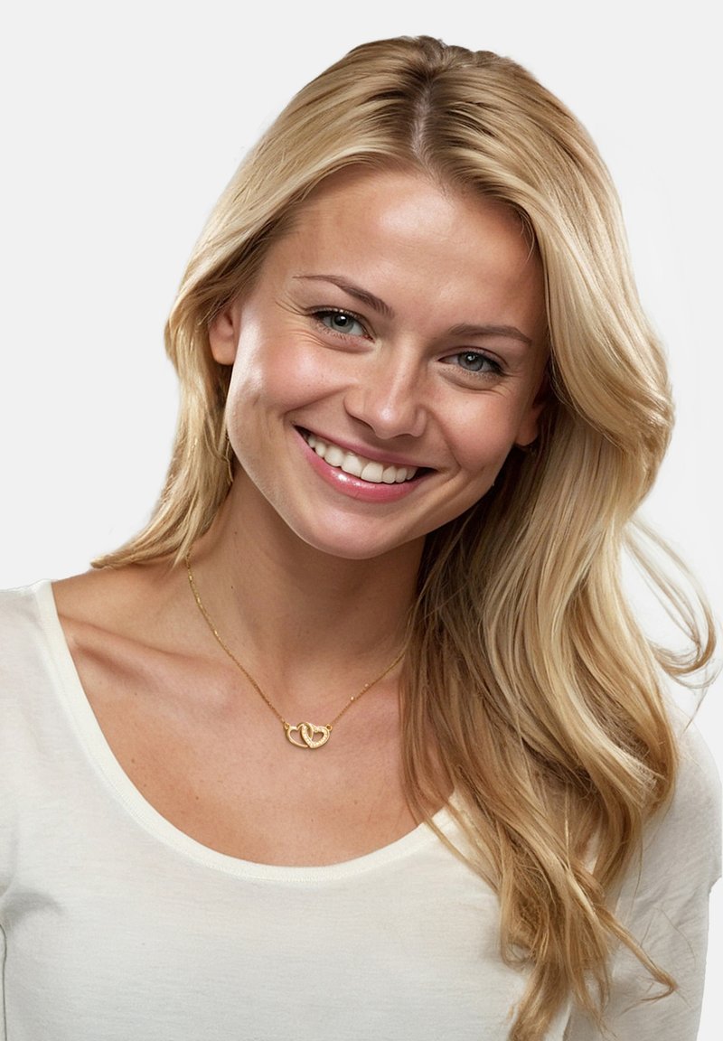 Guldkæde med sammenflettet hjerte design, båret over en hvid bluse. Modellen har langt blondt hår og en neutral baggrund.