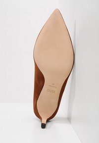 Chaussure à talon haut en daim marron à bout pointu vue par la semelle, avec « HUGO » et la taille 37 imprimés sur la semelle.