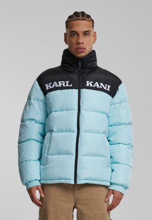 Lyseblå pufferjakke med sort krave, forsynet med hvid "KARL KANI" logo, quiltet design og elastiske manchetter. Lynlåslukning foran.