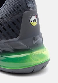 Κοντινό πλάνο στη φτέρνα ενός σκουρόγκρι αθλητικού παπουτσιού Nike Air Max με υφή στο επάνω μέρος και διαφανές έντονο πράσινο αεριζόμενο πέλμα.