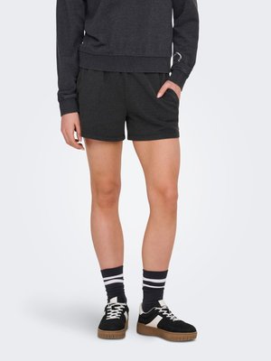 Personne portant un short noir, un sweat-shirt noir, des chaussettes noires avec des rayures blanches, et des baskets noires avec des accents blancs et des semelles marron.