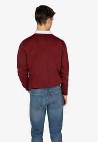 Sudadera de color marrón con cuello redondo y mangas largas, combinada con unos jeans de color azul claro. La tela parece suave con una textura mínima.