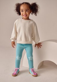 Felpa beige chiaro con finitura testurizzata, abbinata a leggings turchese con toppe a forma di stella azzurro chiaro e sneakers alte multicolori.