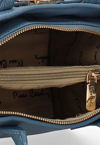 Interno di una borsa di pelle blu con una cerniera dorata, caratterizzato da un compartimento beige e un motivo con logo stampato sull'imbottitura.