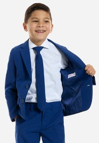 Blauwe pak met een twee-knopen jasje, bijpassende broek en een lichtblauw overhemd. Heeft een stropdas, open jasje waardoor een satijnen binnenkant zichtbaar is.