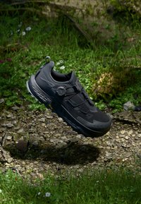 Black athletic shoe with a textured upper, lace-free design, and a round dial closure. Features a cushioned sole and rugged tread pattern.