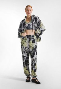 Traje deportivo colorido que incluye un top corto y pantalones holgados con un patrón floral en negro, blanco y verde. Hecho de tela ligera.