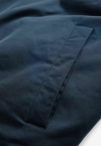 Material bleu marin cu o textură netedă, dotat cu un buzunar discret, unghiular și cusături întărite pe margini.