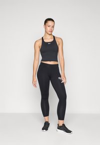 Svart atletisk crop top og tights, begge laget av elastisk stoff. Toppen har et logo, mens tightsene har en sideaksel med et merke-logo.