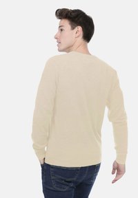 Pull léger beige à manches longues, encolure ronde et coupe ajustée, vu de dos, associé à un jean foncé.