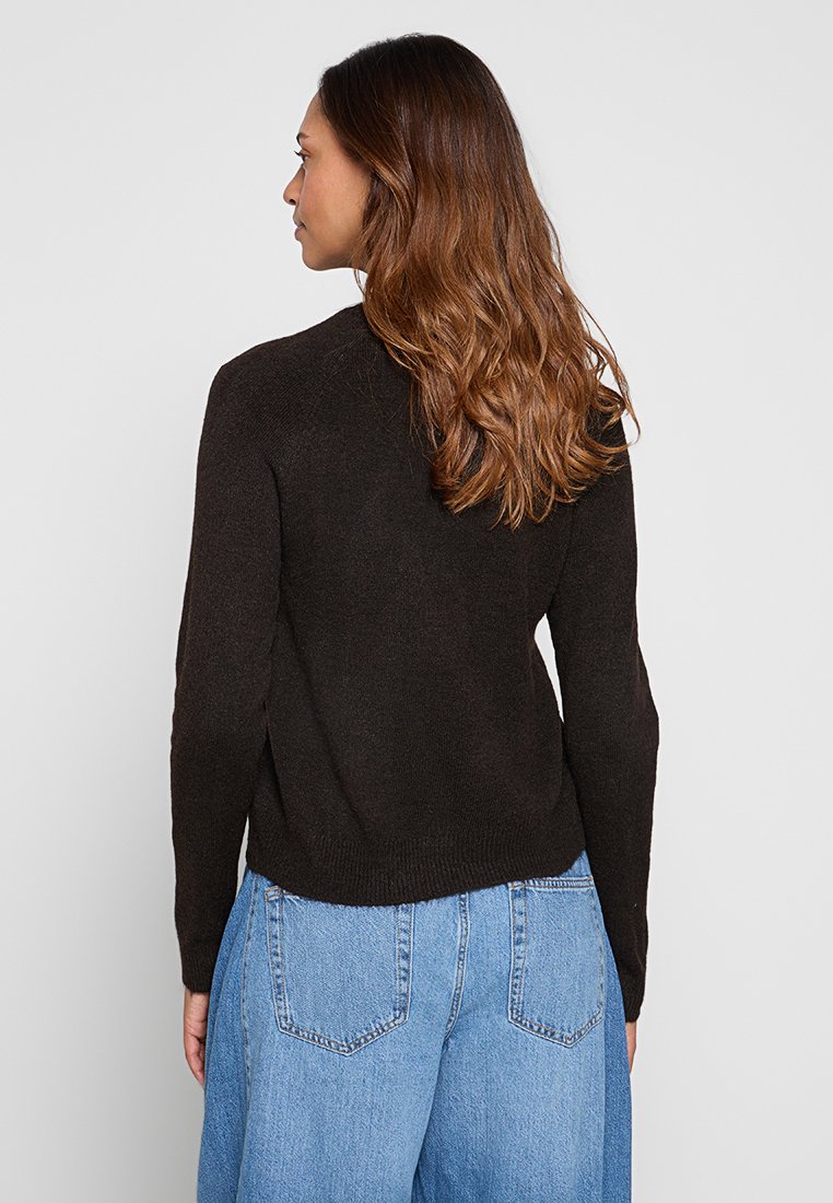 Pull en maille marron foncé à manches longues, avec un col rond et un ourlet côtelé. Porté avec un jean en denim bleu clair.