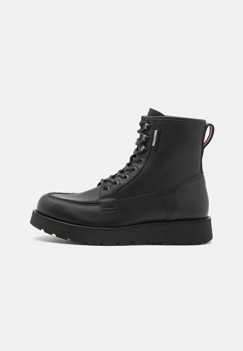 Schwarze Leder Schnürstiefelette mit dicker Sohle, Markenetikett an der Seite und Zugschlaufe an der Ferse, im Profil vor einem weißen Hintergrund dargestellt.