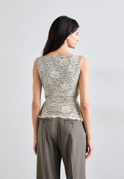 Vaaleanharmaa pitsinen peplum-toppi, jossa on monimutkaisilla kukkakuviolla ja hapsureunalla, yhdistettynä harmaisiin muotonsa mukaiseen housuihin, joissa on nappikoristeet.