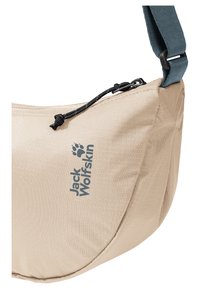 Beige Jack Wolfskin crossbodytas met zwarte ritssluiting en verstelbare blauwe band, met zichtbare textuur van de stof en logo aan de voorkant.
