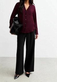 Burgundy button-up shirt with collar and chest pocket, paired with high-waisted black wide-leg trousers and pointed black heels.