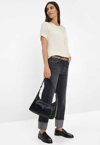 Black leather shoulder bag with a smooth texture, rounded shape, and a single strap, paired with a light cream blouse and dark denim jeans.