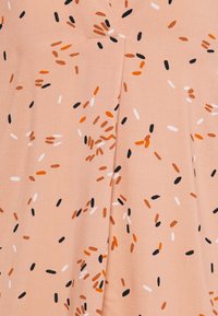 Pezší látka s rozptýlenými, malými oválnými vzory v oranžové, černé a bílé. Materiál má hladkou texturu a mírný lesk.