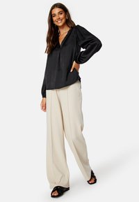 Blusa nera di satin con scollatura profonda a V, maniche lunghe a palloncino, abbinata a pantaloni cremosi a gamba larga e sandali neri. Elegante e dalla vestibilità su misura.
