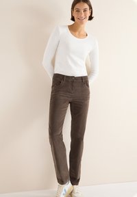 Bruine corduroy broek met een relaxte pasvorm, slanke pijpen en voorzakken. Gecombineerd met een aansluitend wit overhemd met lange mouwen en casual sneakers.