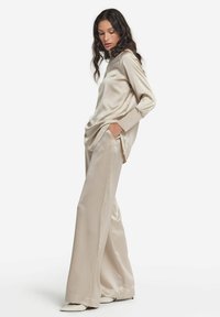 Beige satin Langarmoberteil kombiniert mit weiten Satin-Hosen. Das Outfit hat eine lässige Passform und einen dezenten Glanz, mit seitlichen Taschen in den Hosen.
