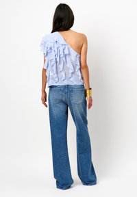 Lichtblauwe top met één schouder en gerimpeld gelaagd stof, gecombineerd met loszittende blauwe spijkerbroek met een vervaagde wasbeurt en een subtiele glans.