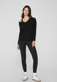 Schwarzes Langarmoberteil mit schulterfreiem Design, kombiniert mit schwarzen Leggings. Das Outfit hat einen lockeren Schnitt und eine glatte Textur.