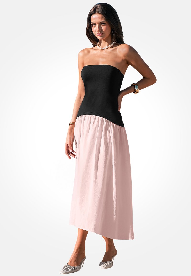 Zwarte strapless corsage gaat over in een vloeiende, gestructureerde roze rok, wat een twee-kleurige maxi-jurk creëert. De schoenen hebben een lichtgekleurde, gerimpelde uitstraling.