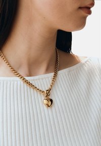 Goldkette mit einem herzförmigen Anhänger. Die Kette hat ein dickes, verlinktes Design, und der Anhänger ist glänzend mit einer glatten Oberfläche.
