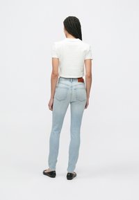 Világoskék, magas derekú, szűk szabású farmernadrág hátul zsebekkel és barna bőr címkével a derékrészen. Fehér, rövidített szabású pólóval viselve.