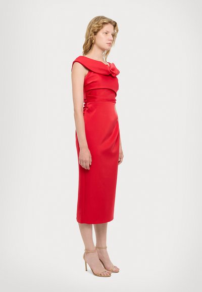 Robe rouge ajustée avec un décolleté structuré hors épaule et un accent floral. Tissu lisse, longueur genou, associée à des talons nus à lanières.
