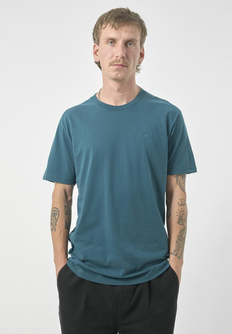 Türkises kurzärmeliges T-Shirt aus weichem Stoff, mit rundem Halsausschnitt und einem dezenten Logo in hellblau auf der Brust gestickt.