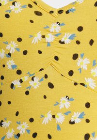 Tecido amarelo com bolinhas pretas e margaridas brancas. Apresenta um design franzido na gola, criando uma aparência texturizada.